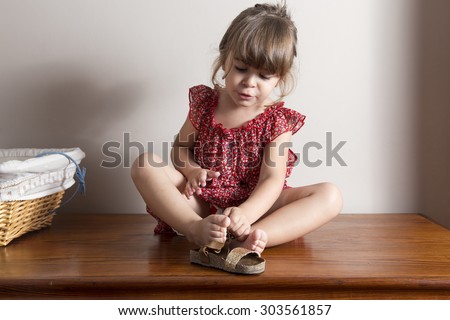 Little girl trying to put on her shoes. Indoor portrait with blank space to put your own text