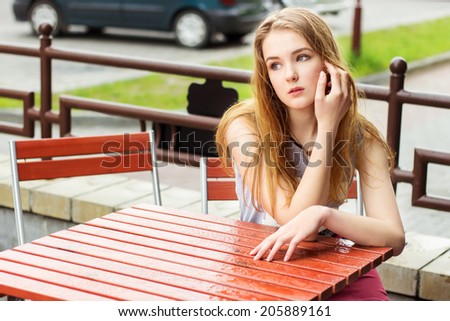 beautiful young woman with long red hair sitting in a cafe on the street in the city after a rain and waiting for my coffee