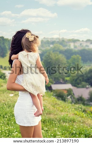young mother with a small daughter in his hands standing on the edge of the cliff and looks into the distance over the city on a summer day