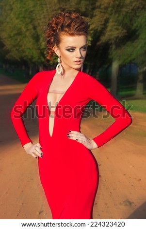 beautiful elegant girl with beautiful makeup and hair in a red evening dress in the Park