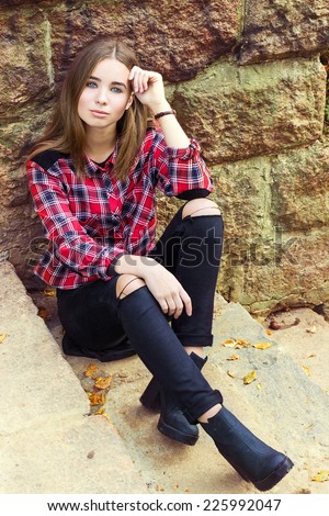 beautiful charming young attractive girl with large blue eyes with dark long hair in autumn day sitting on the stairs in black pants and shirt