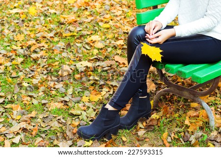 beautiful legs girl in black pants and boots with yellow leaves in the hands of sitting on the bench in autumn Park