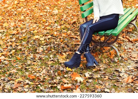 beautiful legs girl in black pants and boots sitting on the bench in autumn Park
