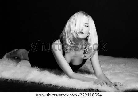 beautiful sexy elegant striking blonde woman with bright makeup red lips in a black dress lies on the white fur in the Studio on a black background