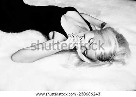 beautiful sexy happy girl blonde with a smile lying on the white carpet in a black dress
