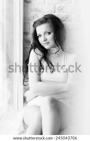 black and white photo of a beautiful sexy girl with long dark hair in a white body sits at home by the window