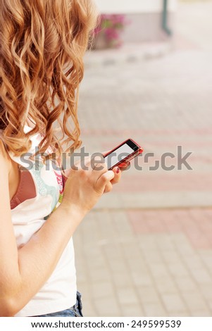 beautiful girl with curly hair standing on the street in phone in hand, sends an SMS message reads