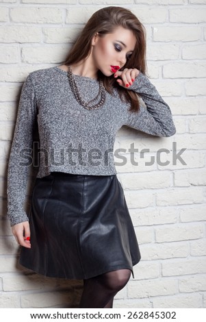beautiful young sexy girl with plump red lips with a red lacquer on the nails in a black leather skirt with a stylish haircut stands near brick wall
