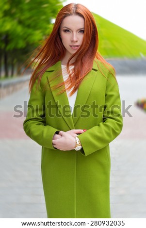 beautiful sexy woman with fiery red hair with green coat walking through the streets of the city