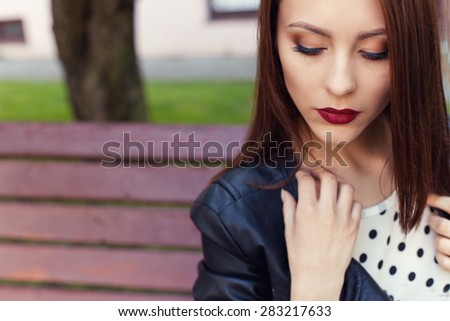 beautiful stylish girl in a black leather jacket with dark lipstick and makeup in the city on the bench