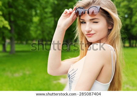 Beautiful cute happy sexy girl with blond long hair in white T-shirt lifted sunglasses and winked