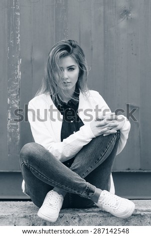 beautiful girl sitting on the ground near the wall in jeans and a white blouse , her hair develops wind
