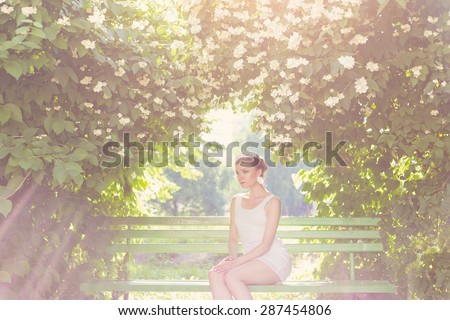 beautiful delicate elegant woman bride in white dress with hair and tiara on his head sitting in a lush garden on a bench under the jasmine in luchas sun , romantic toning