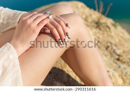 beautiful long legs on the shore of the blue lake , lie the hands on the knees with long acrylic nails