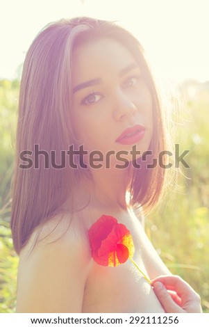 beautiful sexy girl with plump lips with a poppy flower in the hand with bared shoulders at sunset in a field in the sunlight , shading in warm colors