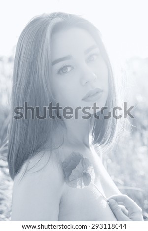 black and white portrait beautiful sexy girl with plump lips with a poppy flower in the hand with bared shoulders at sunset in a field in the sunlight , shading in warm colors