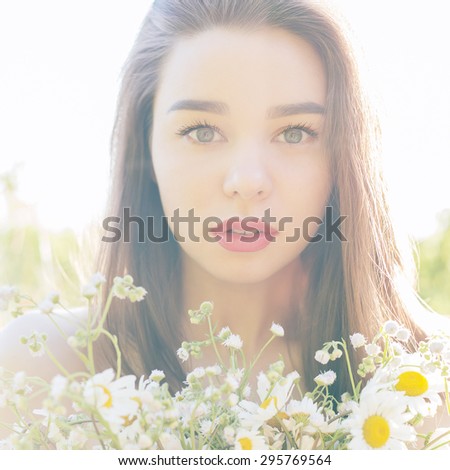 beautiful sexy cute girl with big lips and red lipstick with bared shoulders with a bouquet of daisies at sunset on a sunny warm summer day, the rays of light into the camera