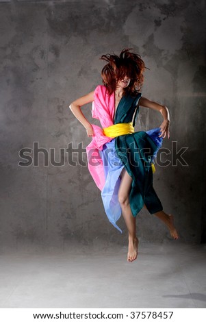 Young modern dancing girl in colorful dress on the dirty grunge  grey studio background