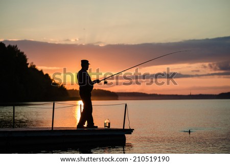 man fishing on a lake from the bridge at sunset