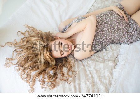 young pregnant woman smiling lying on the bed and touching belly