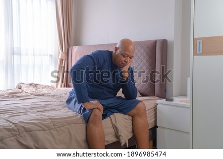 Depressed lonely old elderly black man. African American people sitting on bed with windows in bedroom at home in early morning. Quarantine lifestyle. Unhappy life.