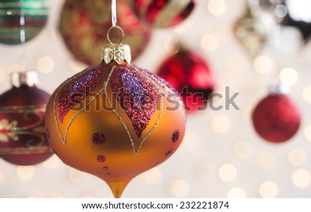 A variety of colorful blown glass Christmas tree ornaments hanging from silver tinsel.  White lights out of focus in the background.