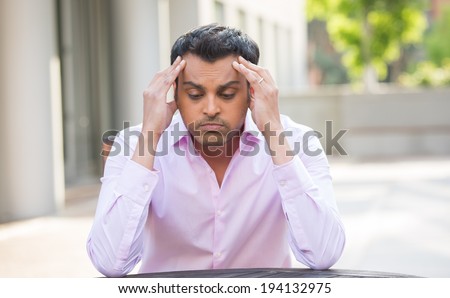 Closeup portrait, stressed young businessman, hands on head with bad headache, isolated background of trees, buildings, outside. Negative human emotion facial expression feelings.