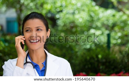 Closeup portrait, friendly, young smiling confident female doctor, healthcare professional talking on phone, isolated outside green trees background. Patient visit health care reform. Positive emotion