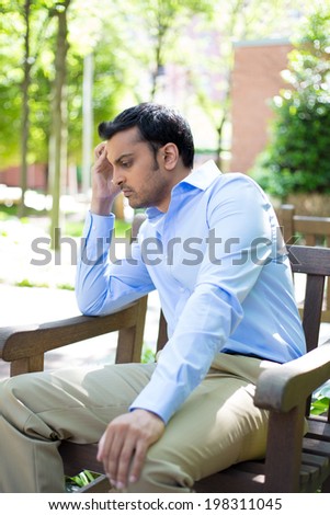 Closeup portrait, stressed young business man, hand on head, worried, isolated background of trees outside. Negative human emotion facial expression feelings.