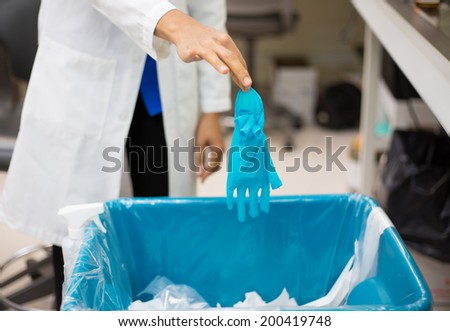 Closeup cropped portrait, healthcare professional throwing away blue disposable latex gloves in trash.  Infection control protocol. Isolated lab background