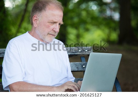Closeup portrait, senior mature man in white shirt typing away, browsing digital computer laptop, isolated background of sunny outdoor, green trees nature background