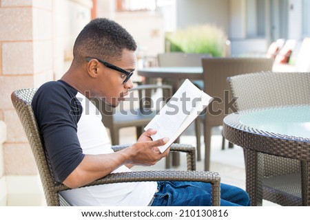Closeup shot, computer geek young man with black glasses sitting down in chair, shocked with funny face by story plot he reads, isolated outdoors outside background. The plot thickens.