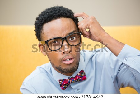 Closeup portrait, young befuddled, bewildered computer geek with big black glasses and bow tie, scratching head wondering about something.
