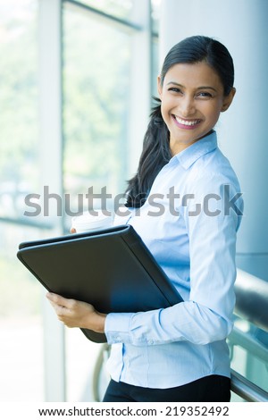 Closeup portrait, young professional, beautiful confident woman in blue shirt, holding coffee and black notebook, smiling isolated indoors office background. Positive human emotions