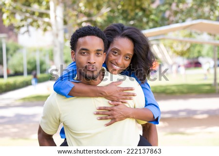 Closeup portrait of a young couple,guy giving woman piggy back ride, happy moments, positive human emotions on isolated outdoors outside park background.