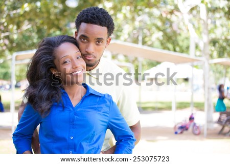 Closeup portrait of a young couple, guy in yellow shirt holding woman with blue shirt from behind, happy moments, positive human emotions on isolated outdoors outside background.