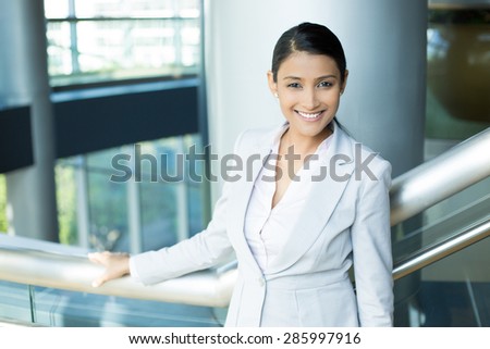 Closeup portrait, young professional, beautiful confident woman in gray white suit, friendly personality, holding rail, smiling isolated indoors office background. Positive human emotions
