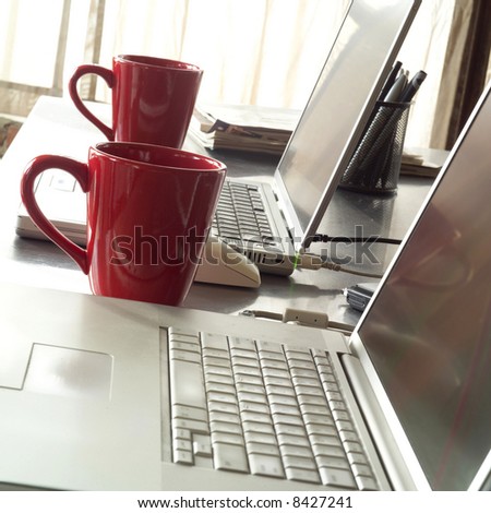 laptop computers on desk with mugs next to window