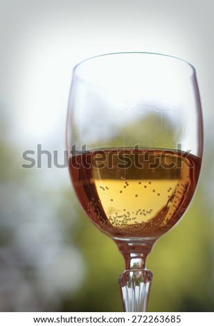 Glass of sparkling wine on a blurred background with sky and foliage of trees.