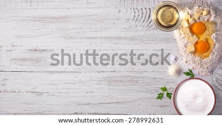 Baking tabletop background with eggs, olive oil, milk, flour, butter on white wooden background
