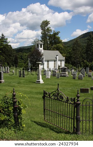 Image of a traditional rural white community church, with graveyard in the foreground, and open gateway leading to the church. Shot in New York State.