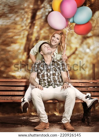 Woman with colorful balloons surprised by a man hugging him from behind  outdoors