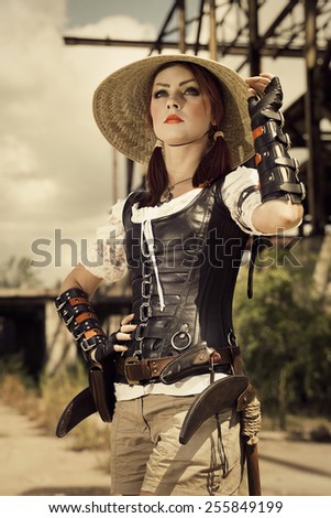 Young steampunk woman in leather corset and vietnam hat  standing on the industrial background.