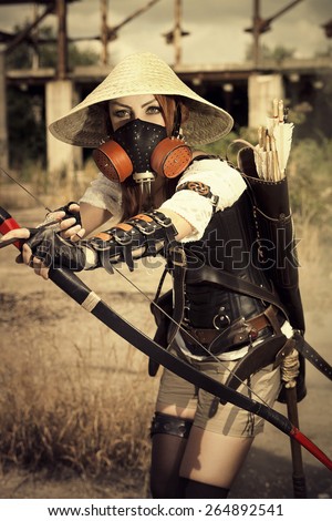 Attractive woman warrior in the mask holding in her hands bow and arrow and arhering.