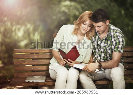 Relationship and education concept. Young  couple of students are sitting on the bench in the park, learning and smiling.