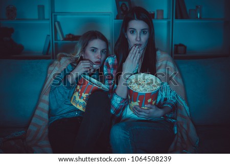 The two women with a popcorn watch a horror film on the sofa 商業照片 © 