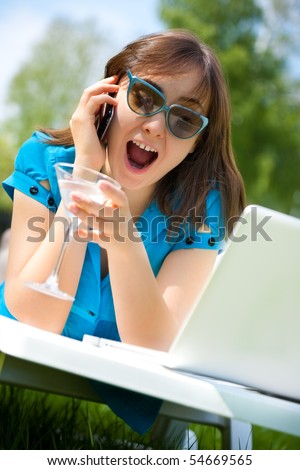 Businesswoman with laptop and glass of martini calling by phone