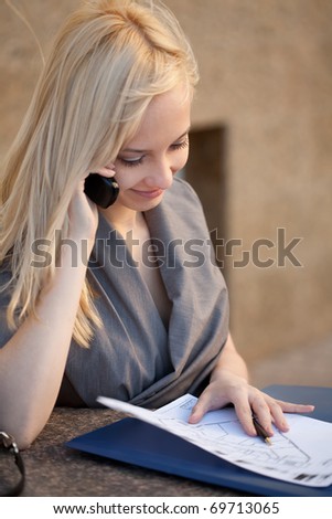 Beautiful woman sitting, calling to phone  and reading documents outdoors