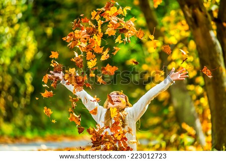 Sitting young girl playfully thrown away over his head colored maple leaves