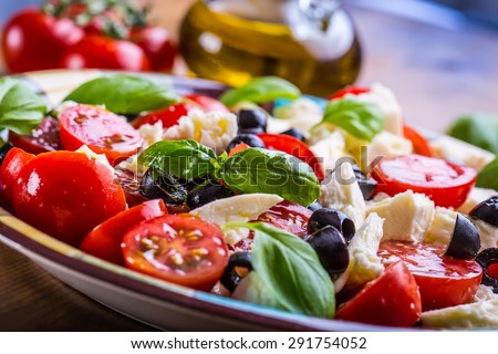 Caprese. Caprese salad. Italian salad. Mediterranean salad. Italian cuisine. Mediterranean cuisine. Tomato mozzarella basil leaves black olives and olive oil on wooden table. Recipe - Ingredients